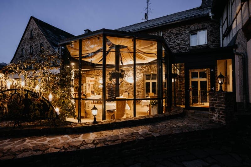 Außenansicht Hotel Hoher Hahn bei Nacht mit beleuchtetem gläsernen Wintergarten und historischer Schieferfassade